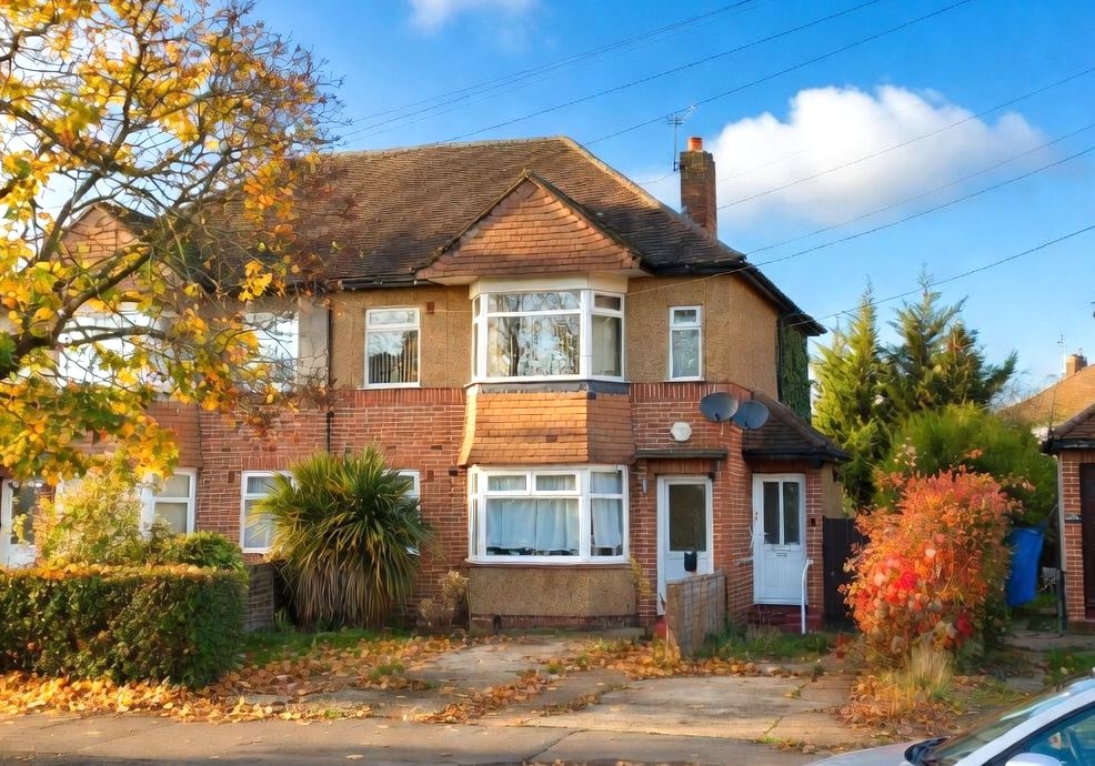 A semi-detached house with an overgrown front garden and autumn leaves across the drive