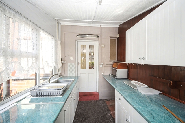An unmodernised kitchen in an inherited house, with dated units and worn flooring