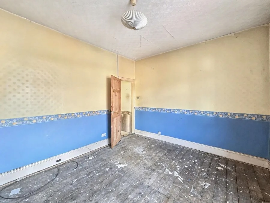 A first floor bedroom with the carpet lifted, floorboards exposed and the original blue and cream wall paper still in place